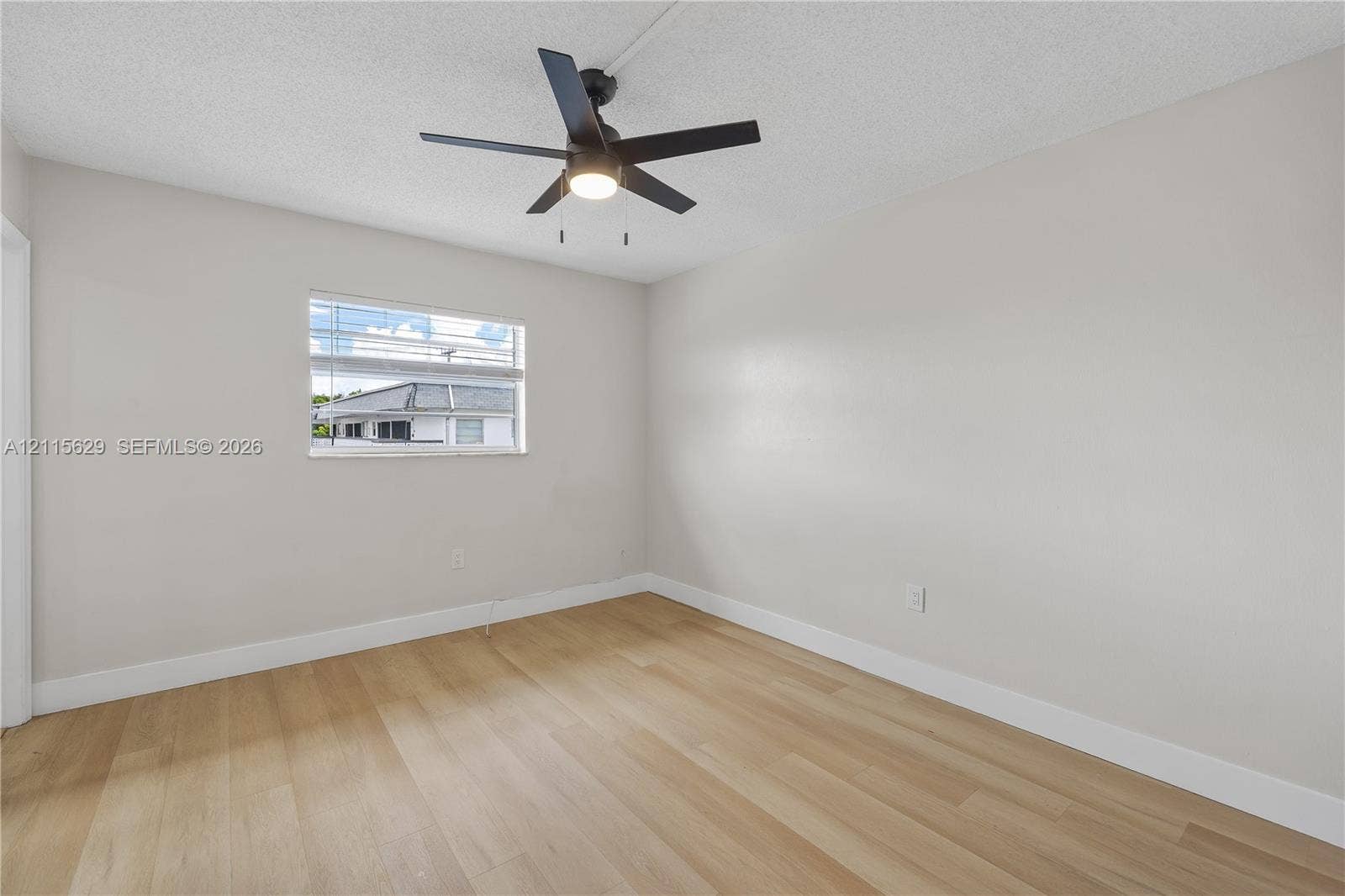 Neutral-toned room featuring light wood-finish flooring, a ceiling fan with integrated lighting, and horizontal window blinds