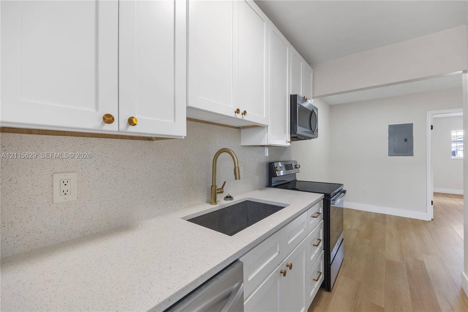 Kitchen featuring white shaker-style cabinetry, solid-surface countertops, gold-tone hardware, a gooseneck faucet with an undermount sink, and wood-finish flooring