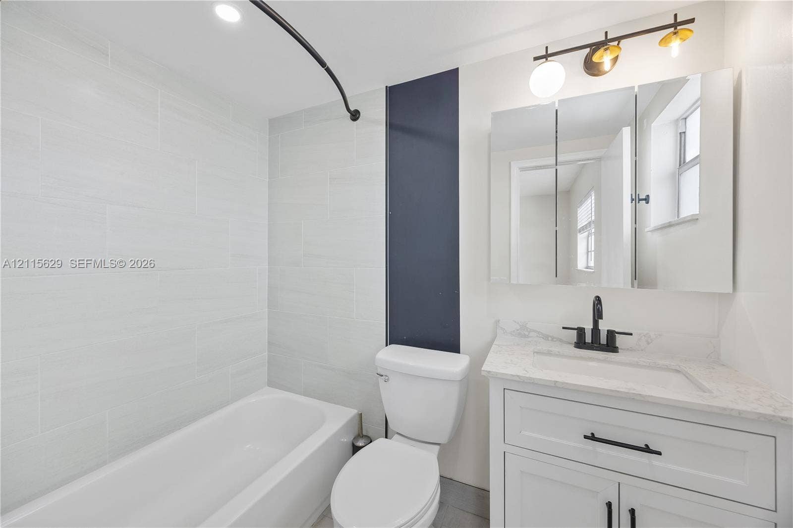 Bathroom featuring a white vanity with stone-finish countertop, matte black hardware, integrated vanity mirror with cabinetry, and tub-shower combination with light-toned wall tile