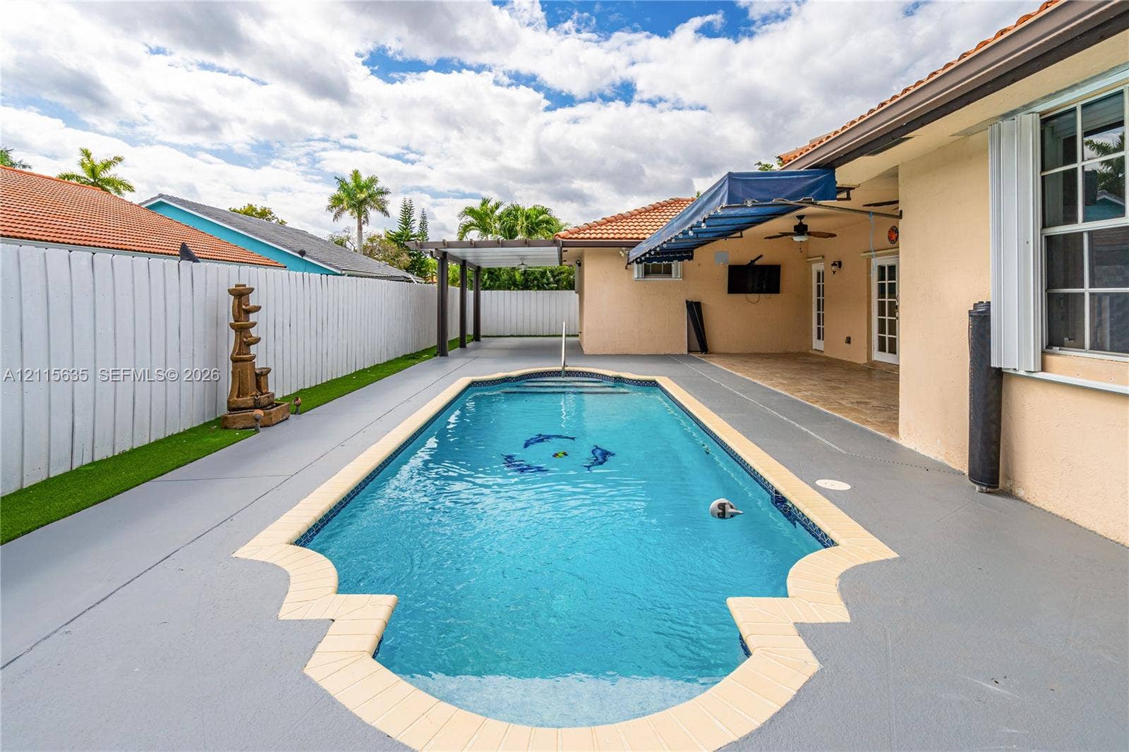 15374 SW 113th Terrace, Miami, FL 33196 In-ground swimming pool with decorative tile coping, covered patio, retractable fabric awning, and enclosed outdoor area with white privacy fencing