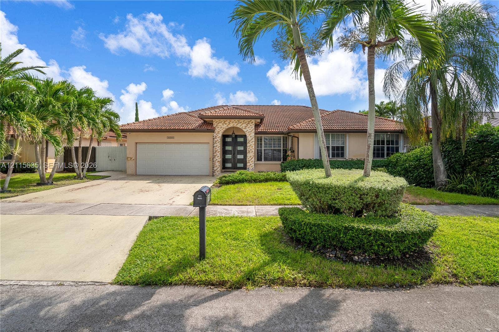 15374 SW 113th Terrace, Miami, FL 33196 Single-story residence featuring a tile roof, decorative stone entryway facade, multi-panel glass front door, two-car garage, and mature landscaping