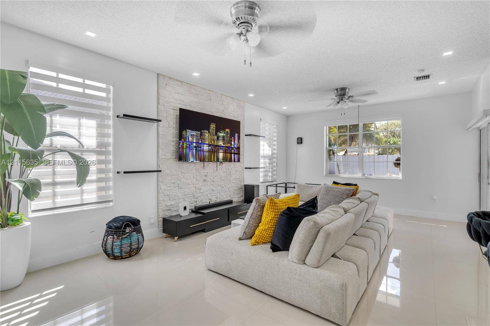 15374 SW 113th Terrace, Miami, FL 33196 Living area featuring a floor-to-ceiling textured stone accent wall, large-format tile flooring, recessed ceiling lighting, and dual ceiling fans