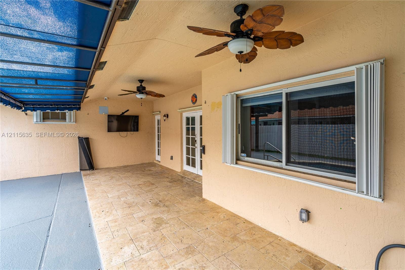 15374 SW 113th Terrace, Miami, FL 33196 Covered patio featuring stone-tiled flooring, dual ceiling fans, a retractable blue canopy, and sliding glass entry doors