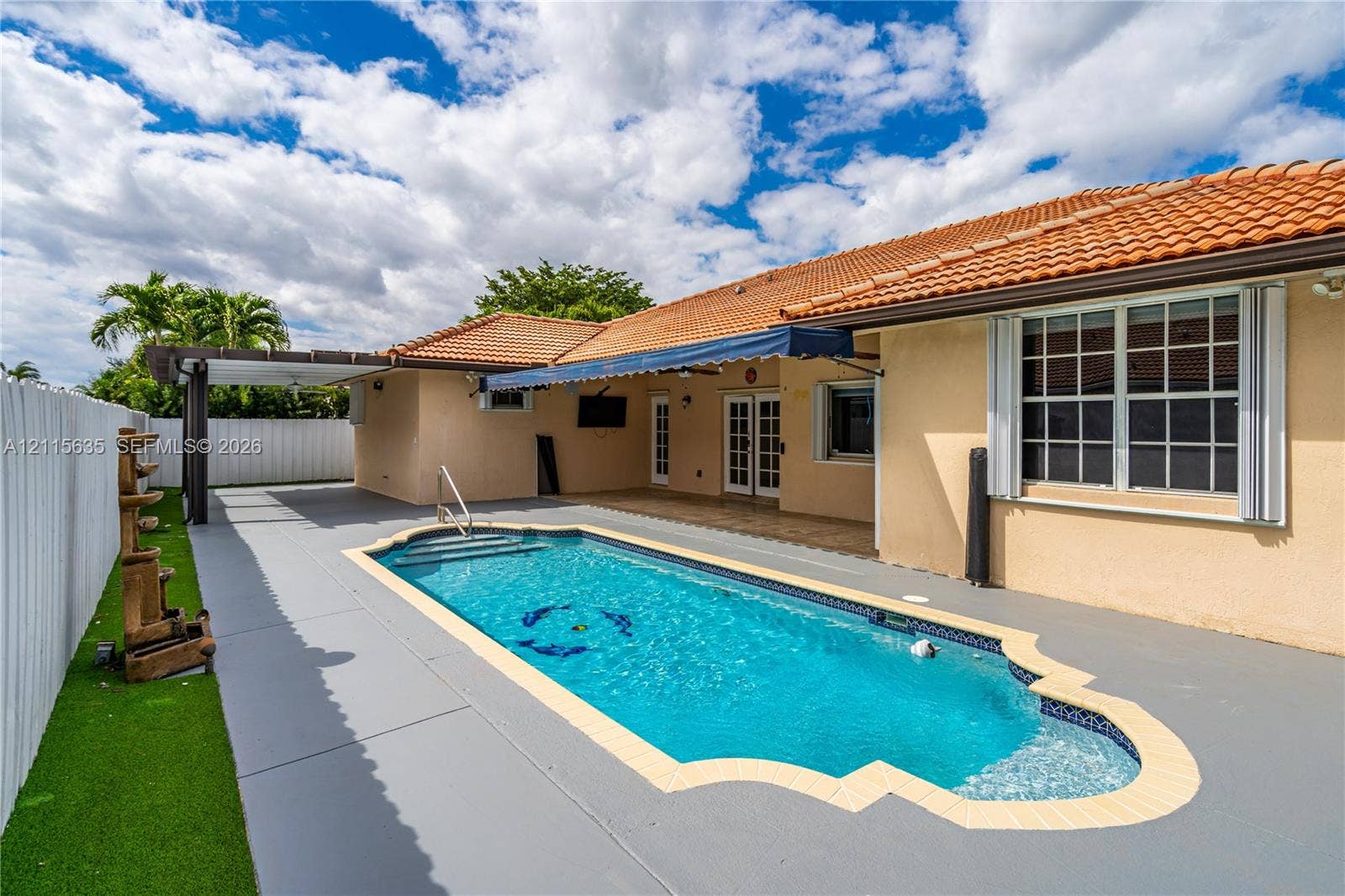 15374 SW 113th Terrace, Miami, FL 33196 In-ground swimming pool with a custom-shaped perimeter, terra cotta tile roof, retractable fabric awning, wooden-frame pergola, and synthetic turf lawn