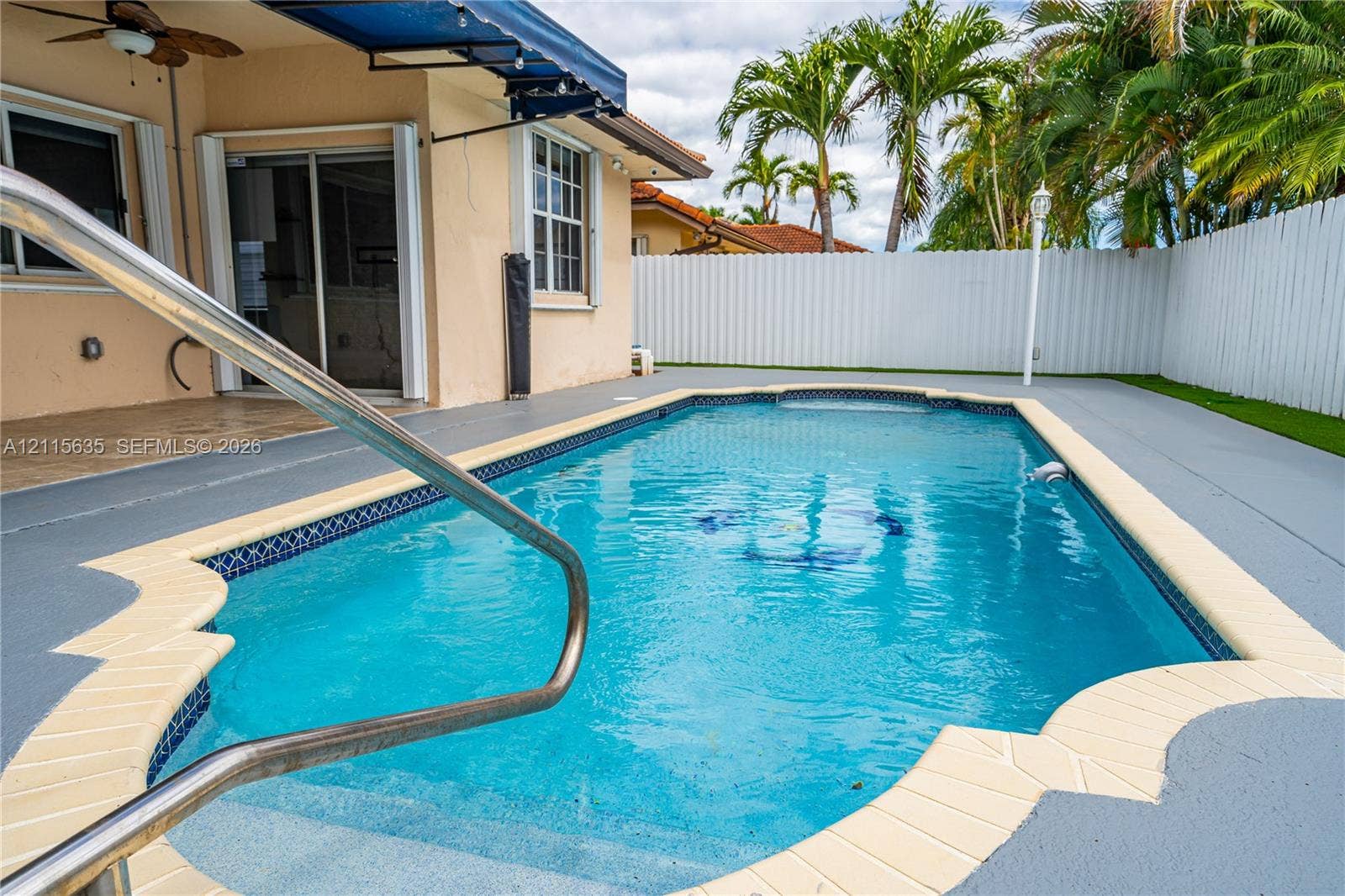 15374 SW 113th Terrace, Miami, FL 33196 In-ground swimming pool with tile border and integrated steps, concrete pool deck, retractable fabric awning, and white privacy fencing