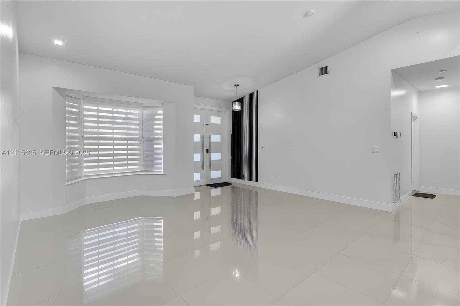 15374 SW 113th Terrace, Miami, FL 33196 Bright interior featuring vaulted ceilings, polished tile flooring, a multi-pane front entry door with vertical handle hardware, and a bay window equipped with horizontal blinds