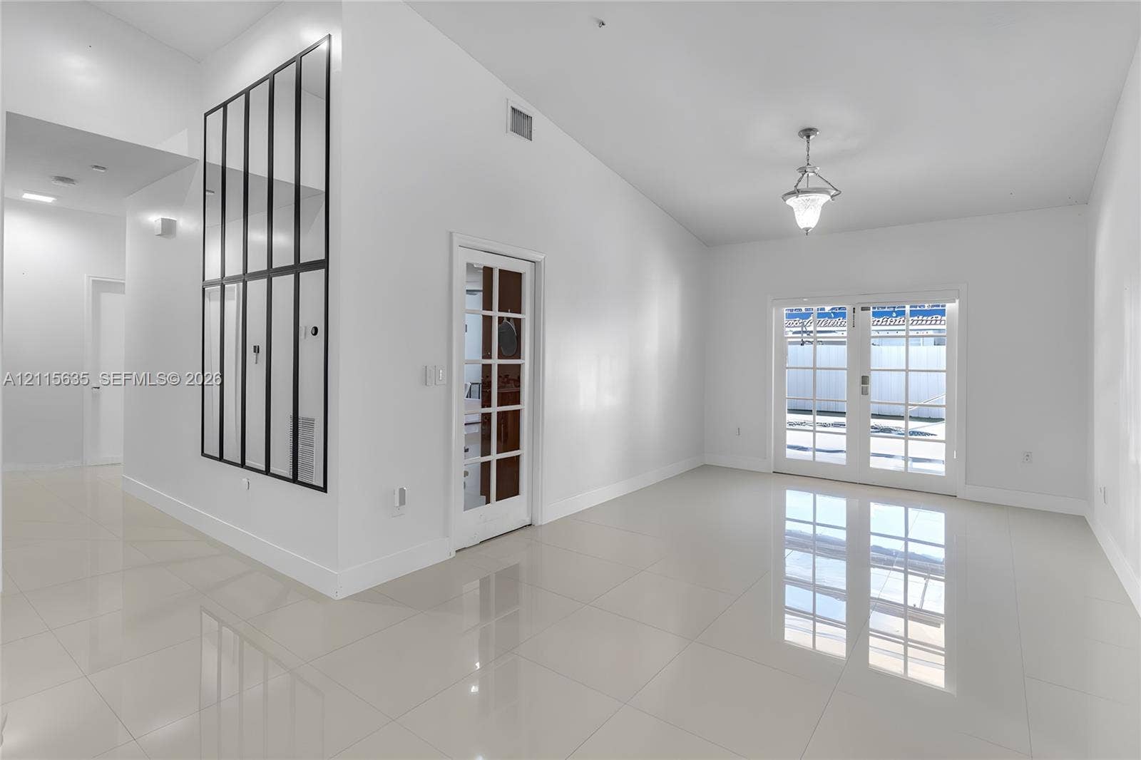 15374 SW 113th Terrace, Miami, FL 33196 Vaulted ceiling, neutral large-format tile flooring, decorative grid-pattern wall mirror, glass-paned interior door, and double glass-paned exterior doors