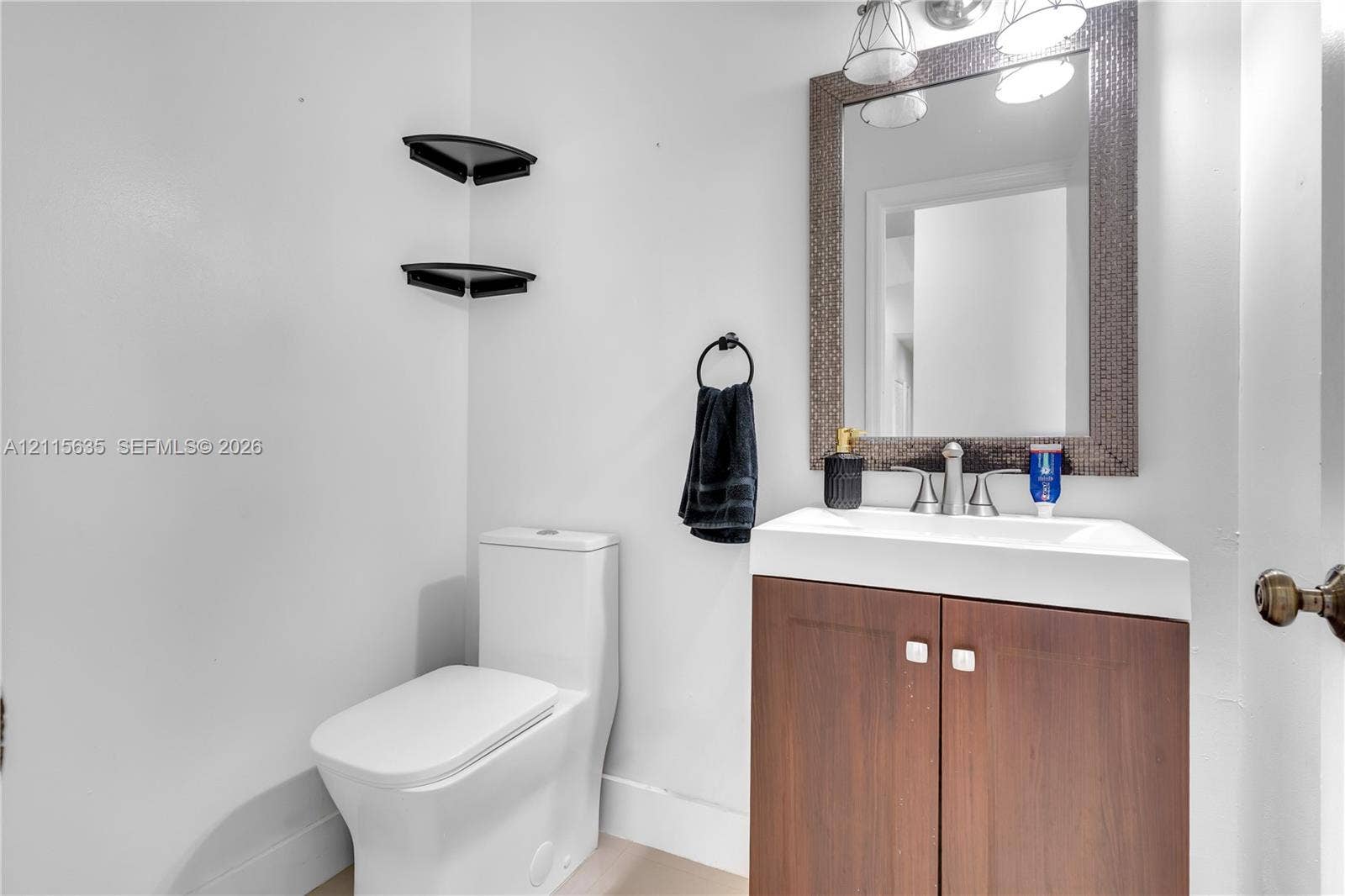 15374 SW 113th Terrace, Miami, FL 33196 Bathroom featuring a wood-finish vanity with a rectangular sink, wall-mounted corner shelving, a framed mirror with integrated lighting, and a modern dual-flush toilet