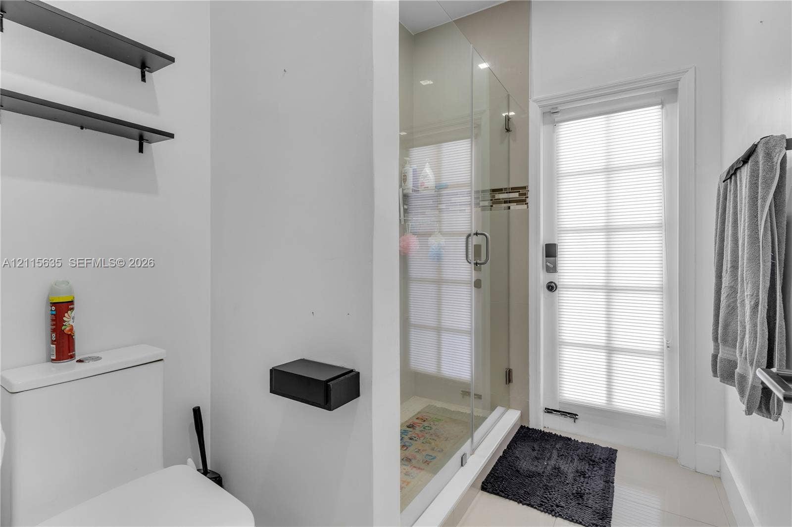 15374 SW 113th Terrace, Miami, FL 33196 Full-height glass-enclosed shower, wall-mounted matte black shelving, matte black wall-mounted toilet paper holder, and a glass-paneled exterior door