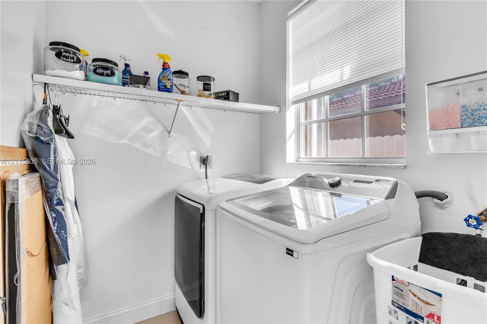 15374 SW 113th Terrace, Miami, FL 33196 Laundry room featuring a single-hung window, white metal shelving, and a wall-mounted multi-compartment dispenser
