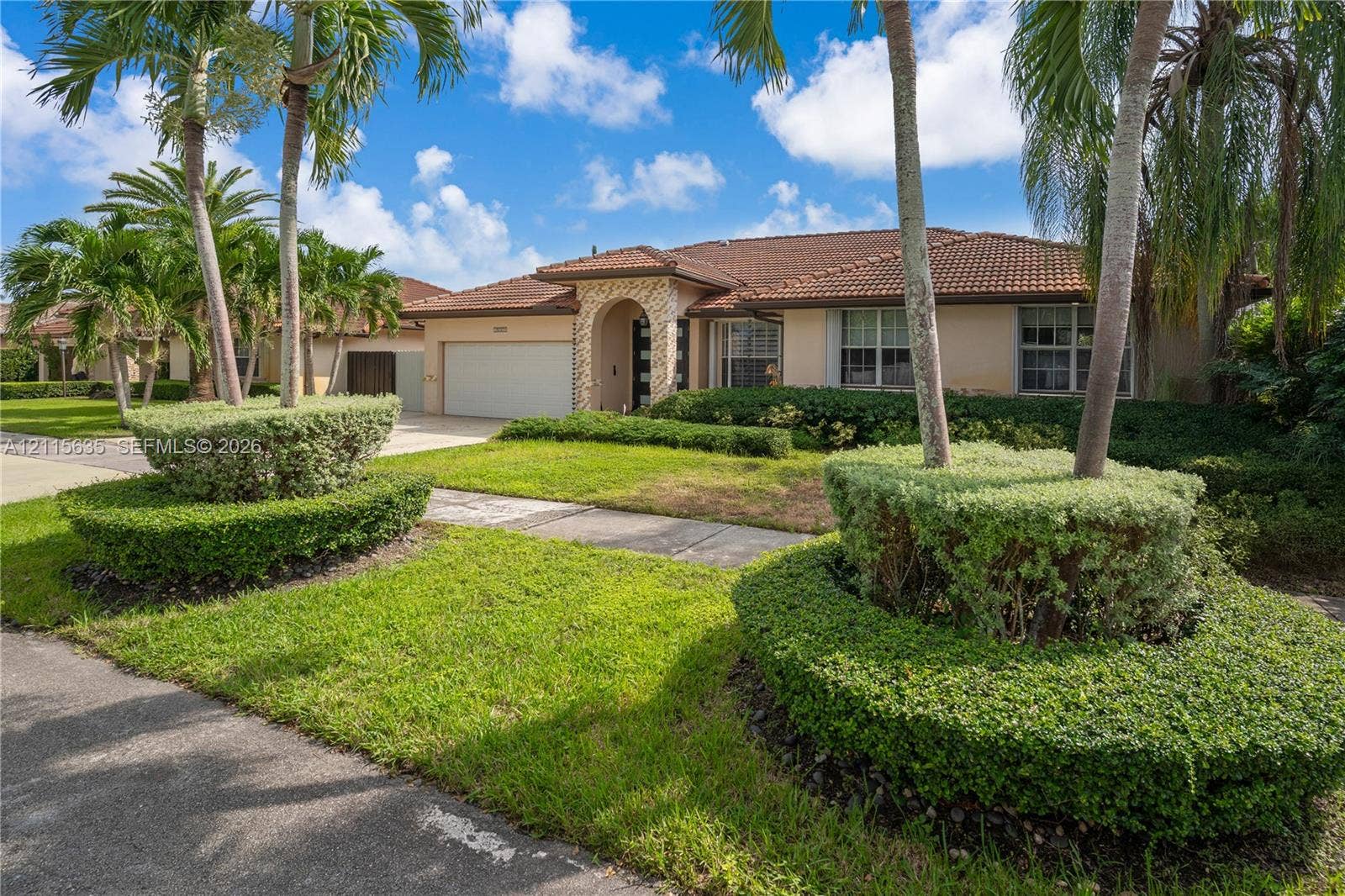 15374 SW 113th Terrace, Miami, FL 33196 Single-story exterior featuring a concrete tile roof, stone veneer entryway, and two-car garage, surrounded by manicured landscaping and mature palm trees