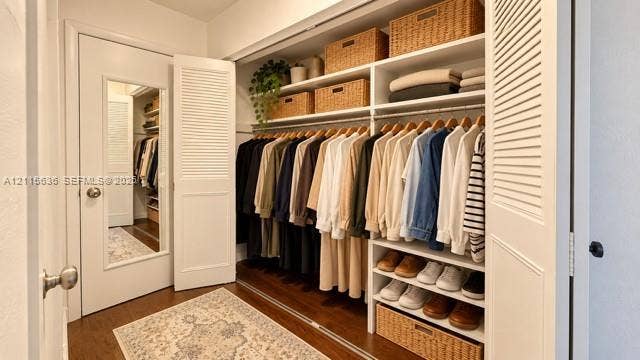 3860 NE 170th Street, #310, North Miami Beach, FL 33160 Walk-in closet featuring wood-finish flooring, built-in shelving, integrated hanging rods, and a door with a full-length mirror