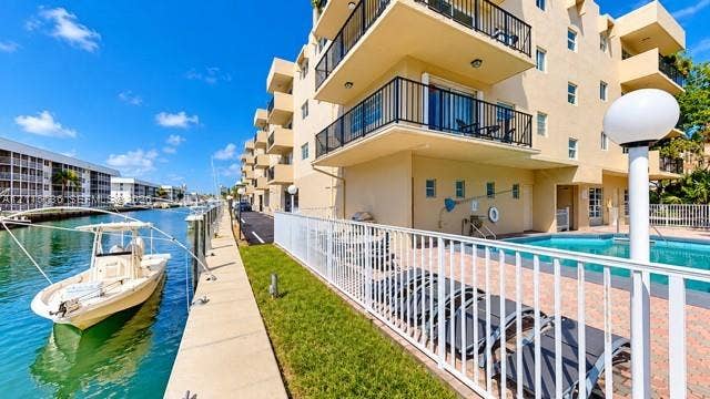 3860 NE 170th Street, #310, North Miami Beach, FL 33160 Waterfront building exterior featuring private boat slips, an in-ground pool with paved deck, and cantilevered balconies with black railings