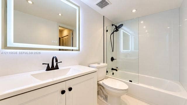 3860 NE 170th Street, #310, North Miami Beach, FL 33160 Bathroom featuring an illuminated wall-mounted mirror, white cabinetry with a solid surface countertop, matte black faucet hardware, and a tub-shower combination with a glass panel enclosure