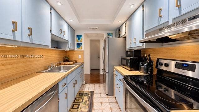 3860 NE 170th Street, #310, North Miami Beach, FL 33160 Galley kitchen featuring light blue cabinetry, gold-tone hardware, wood-finish countertops, stainless steel appliances, and recessed ceiling lighting