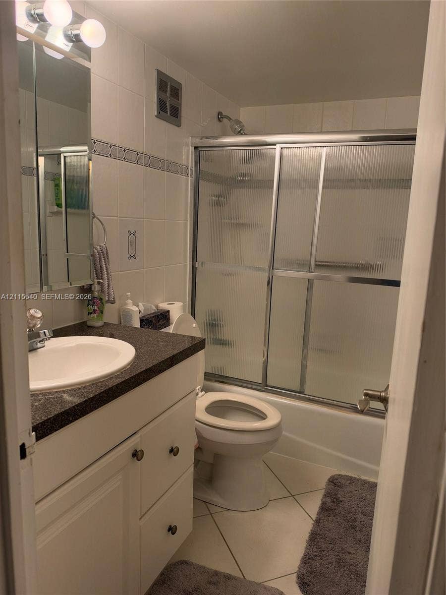 1913 S Ocean Drive, #426, Hallandale Beach, Hallandale Beach, FL 33009 Bathroom featuring white cabinetry, dark stone-finish countertop with an integrated basin, tiled shower surround with sliding glass doors, and tiled flooring
