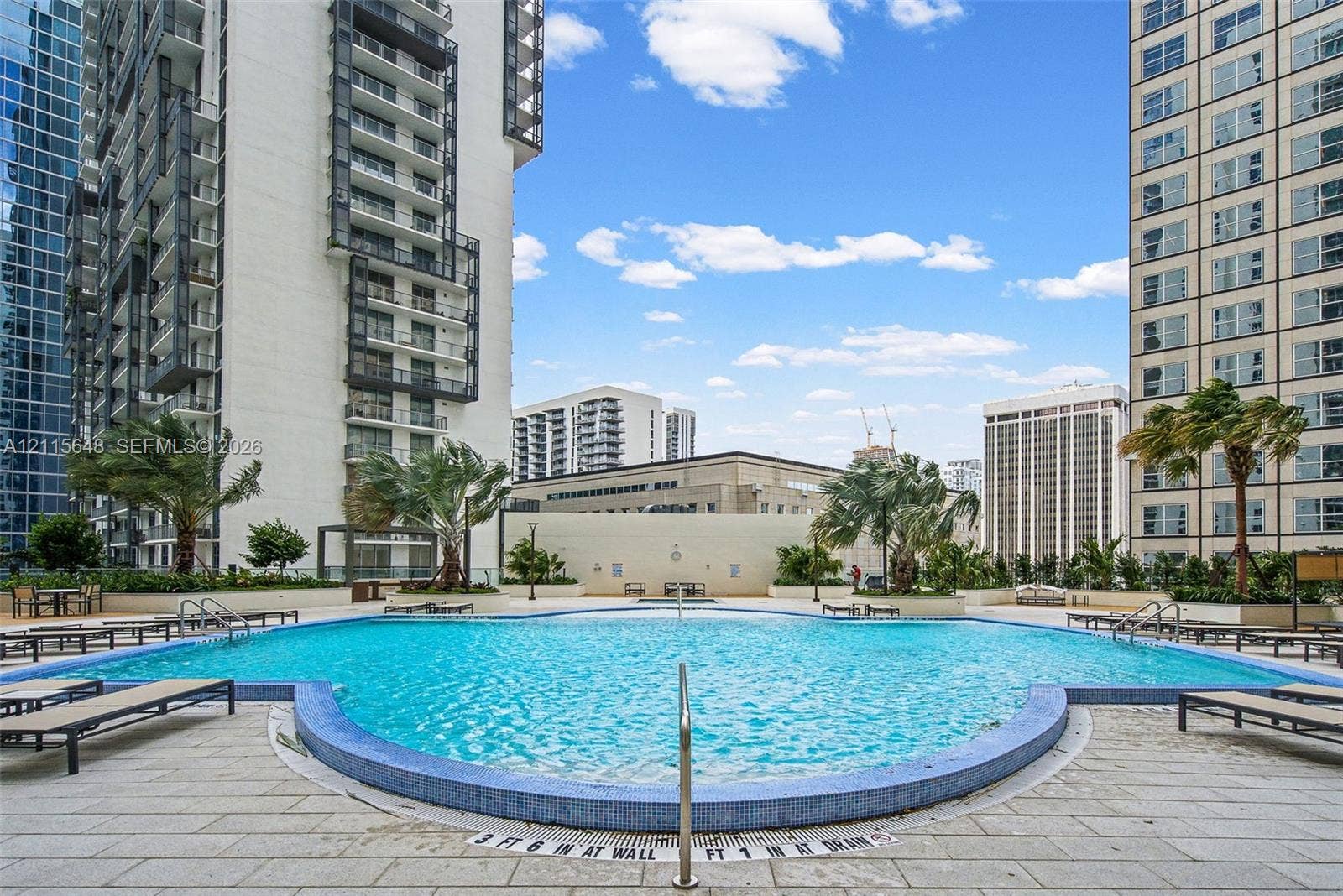 300 S Biscayne Boulevard, #T-3604, Miami, FL 33131 Swimming pool featuring blue tile coping, metallic entry handrails, and a stone-paver pool deck surrounded by integrated landscaping and mature palm trees