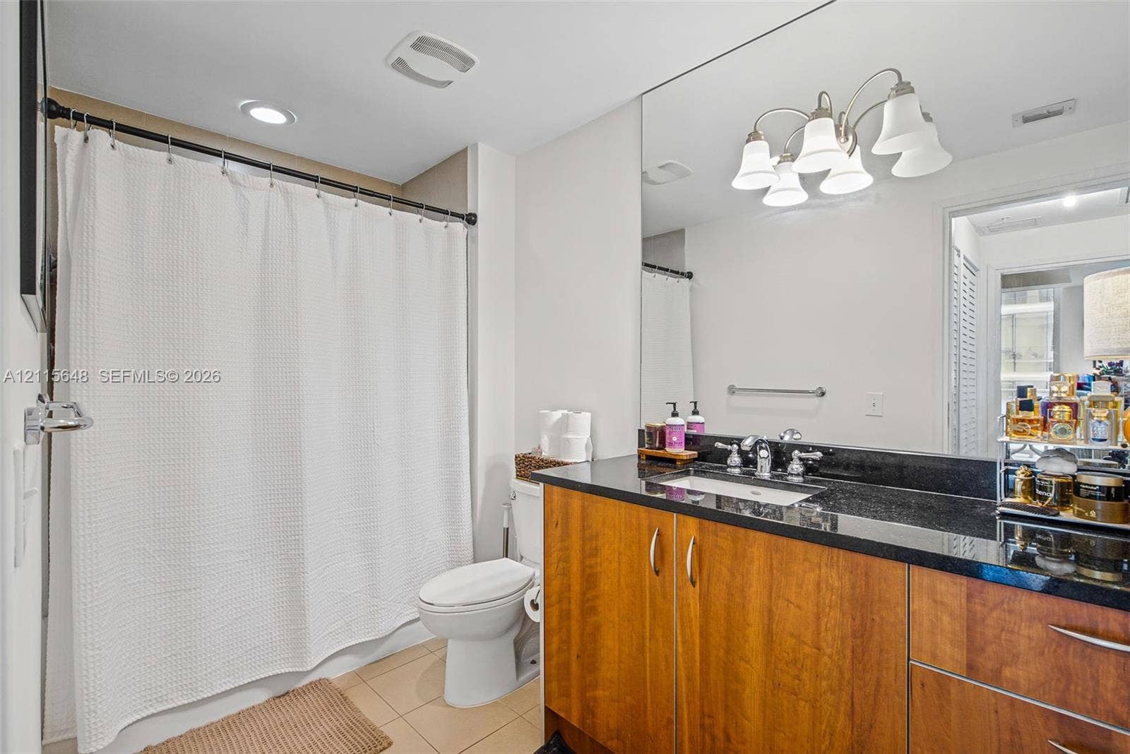 300 S Biscayne Boulevard, #T-3604, Miami, FL 33131 Bathroom featuring a dark-toned stone vanity countertop, wood-finish cabinetry, an undermount sink with dual-handle polished chrome faucet, a full-width wall mirror, and a five-light overhead fixture