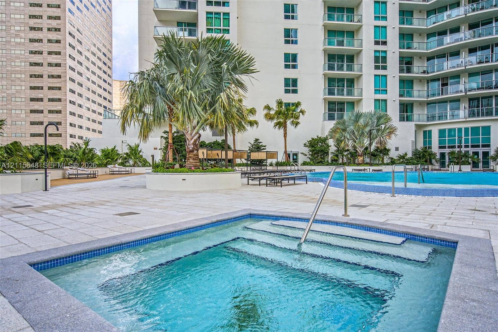 300 S Biscayne Boulevard, #T-3604, Miami, FL 33131 In-ground spa with stone-tile surround, expansive paved pool deck, large swimming pool, mature palm trees, and multi-story high-rise exterior