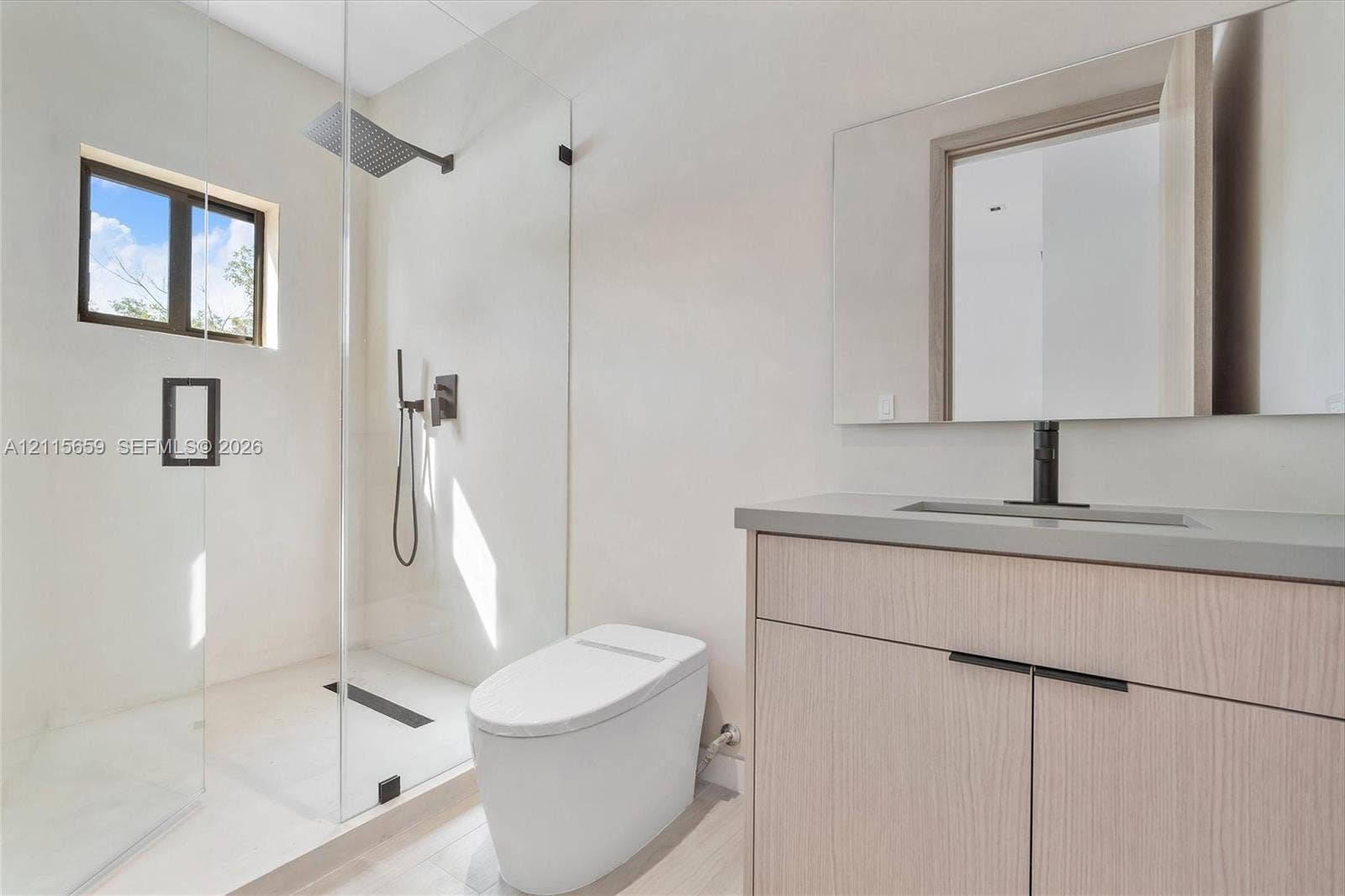 4719 N Miami Avenue, Miami, FL 33127 Modern bathroom featuring a wood-finish vanity, solid-surface countertop, frameless glass-enclosed shower, wall-mounted matte black fixtures, and a sleek rectangular mirror