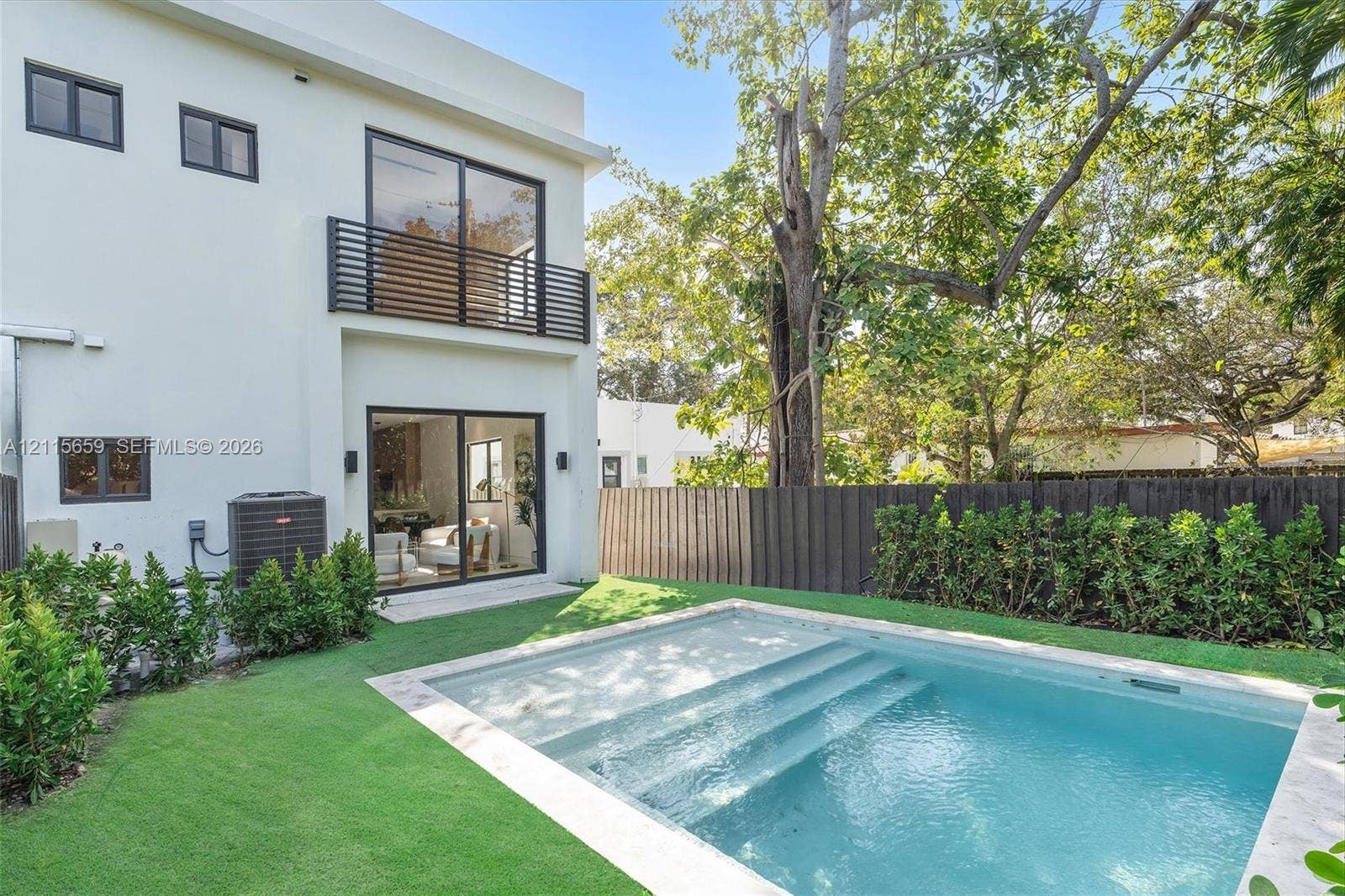 4719 N Miami Avenue, Miami, FL 33127 Two-story stucco exterior featuring a second-level balcony with horizontal metal railing, a swimming pool with integrated stairs, and a manicured lawn