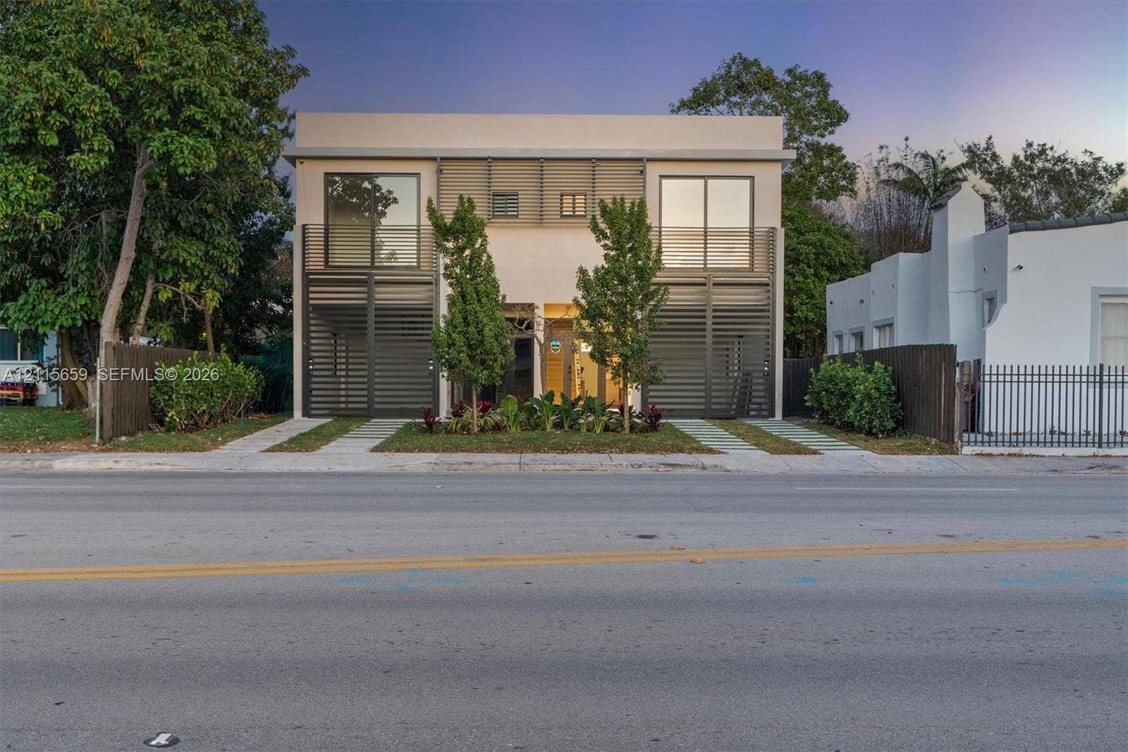 4719 N Miami Avenue, Miami, FL 33127 Contemporary two-story exterior featuring a smooth stucco finish, vertical metal louvers, expansive floor-to-ceiling glass panels, and dual concrete paved driveways
