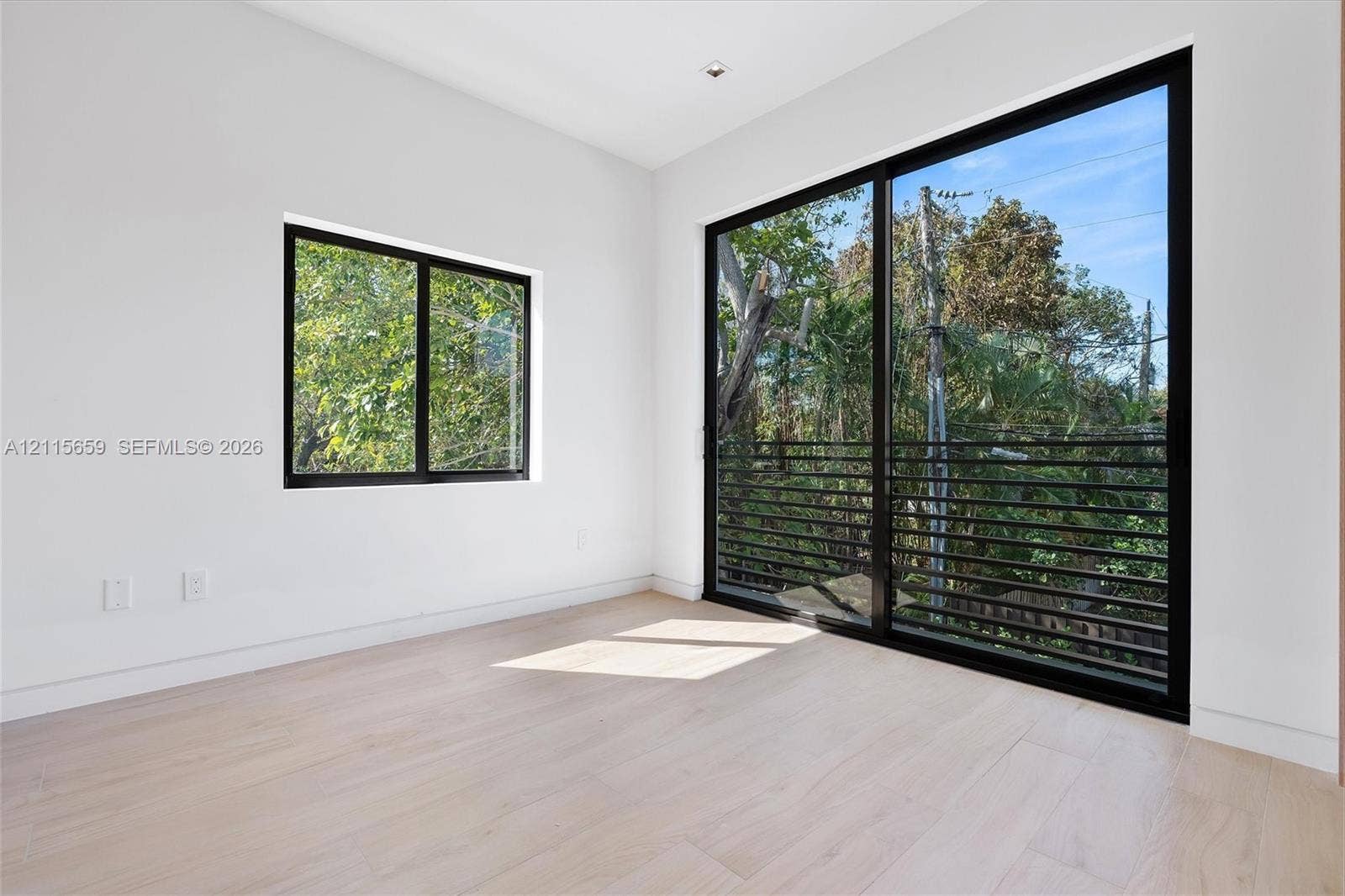 4719 N Miami Avenue, Miami, FL 33127 Neutral interior space featuring wood-finish flooring, floor-to-ceiling sliding glass doors, a secondary window, and matte black framing
