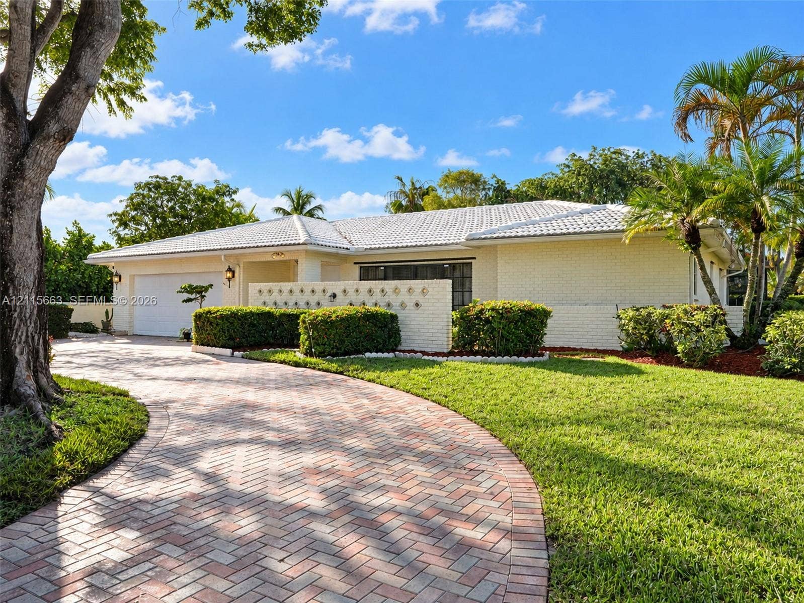 9788 NW 18th Street, Coral Springs, FL 33071 Single-story residence featuring painted brick masonry, a white tile roof, a curved herringbone-patterned brick paver driveway, and integrated decorative screen wall accents