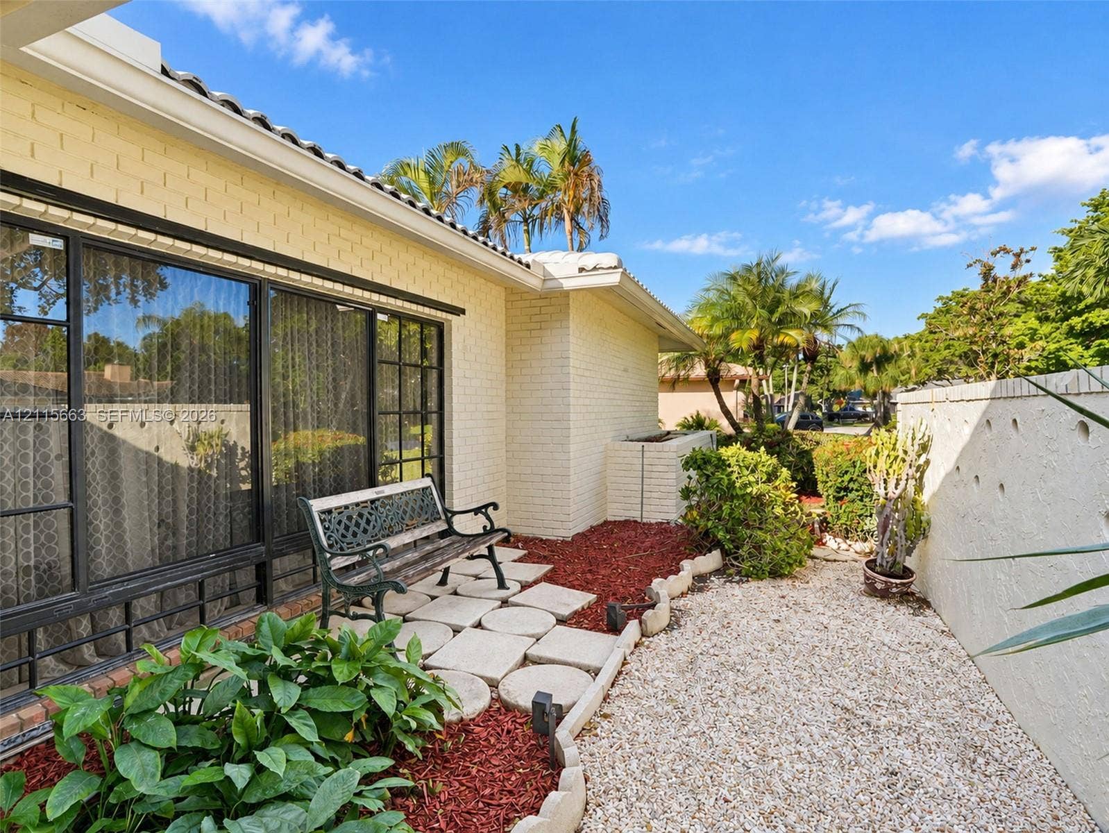 9788 NW 18th Street, Coral Springs, FL 33071 Light-colored brick exterior featuring large-pane metal windows, concrete paver pathway, decorative landscape edging, and low-maintenance gravel ground cover