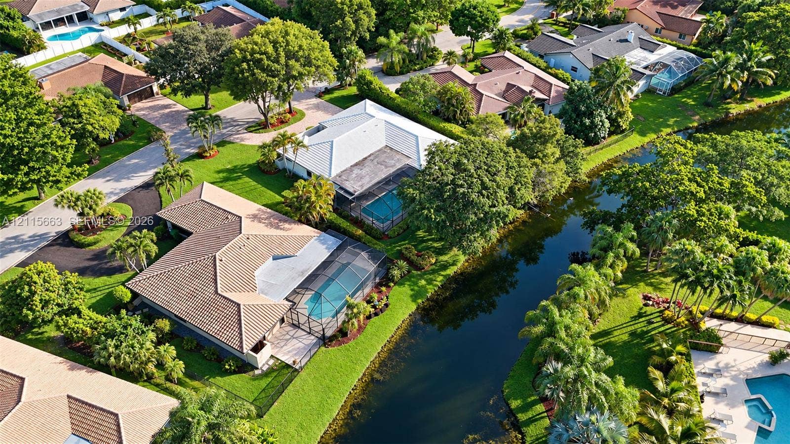 9788 NW 18th Street, Coral Springs, FL 33071 Aerial perspective of a single-story residence featuring a tile roof, an enclosed swimming pool, manicured landscaping, and a canal-front lot