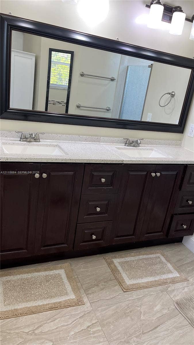 19409 NW 24th Place, Pembroke Pines, FL 33029 Double vanity featuring dark wood cabinetry, solid-surface countertops with dual undermount sinks, a full-width framed mirror, and tiled flooring