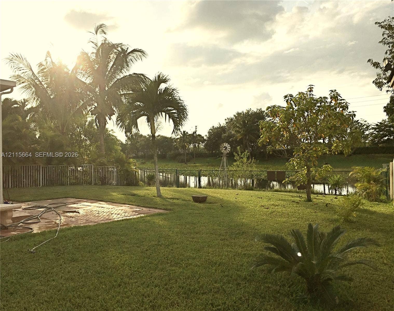 19409 NW 24th Place, Pembroke Pines, FL 33029 Expansive backyard featuring a brick paver patio, metal perimeter fencing, mature palm trees, and waterfront grounds