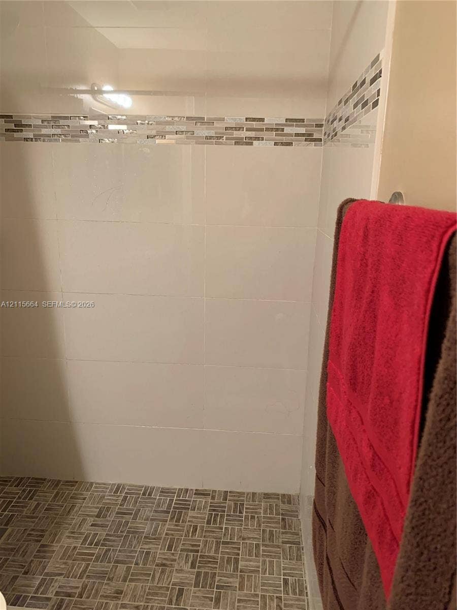 19409 NW 24th Place, Pembroke Pines, FL 33029 Shower stall featuring large-format white wall tile, a decorative glass-blend mosaic accent border, and a patterned tile floor