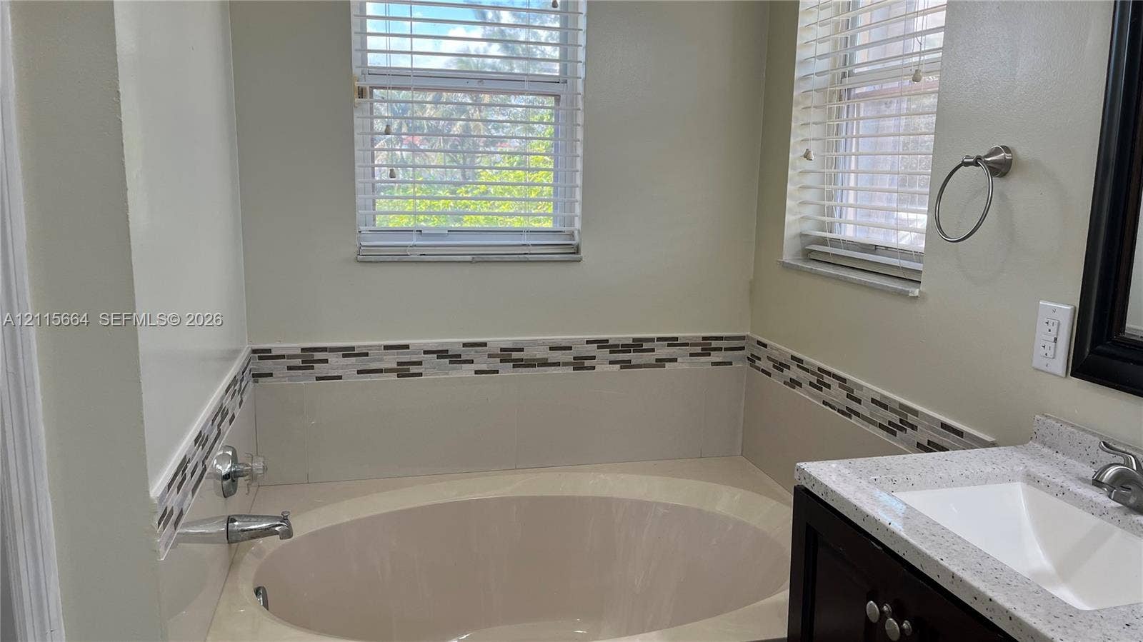 19409 NW 24th Place, Pembroke Pines, FL 33029 Oval soaking tub with chrome hardware, decorative horizontal tile border, stone-finish countertop, undermount sink, and dark wood-tone cabinetry