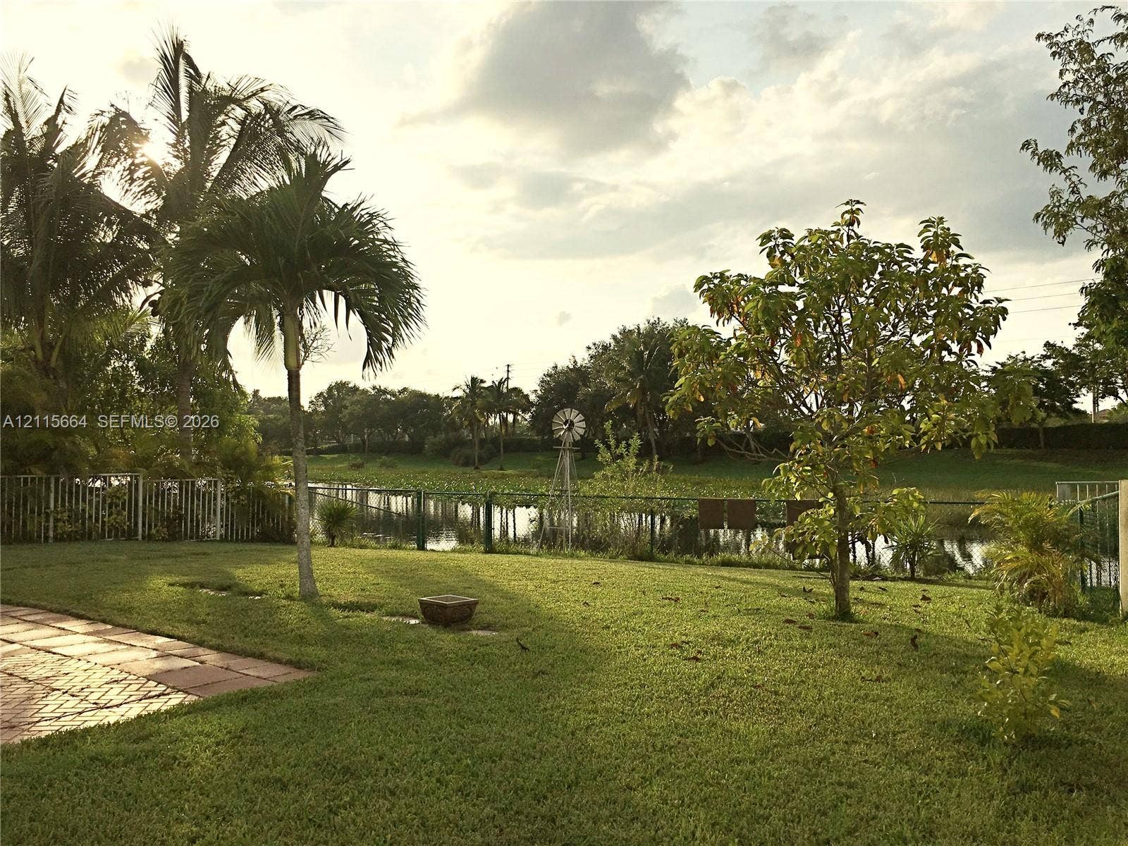 19409 NW 24th Place, Pembroke Pines, FL 33029 Backyard featuring a brick-paver patio, expansive lawn, mature palm trees, perimeter fencing, and water frontage