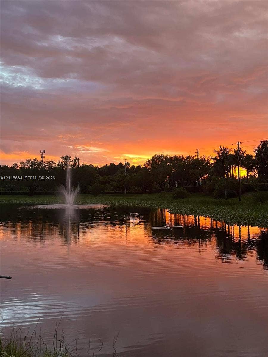 19409 NW 24th Place, Pembroke Pines, FL 33029 Waterfront pond featuring a central fountain, mature perimeter landscaping, and a sunset backdrop