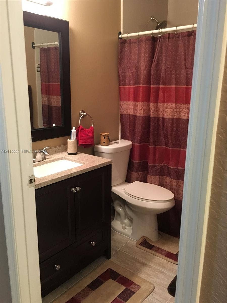 19409 NW 24th Place, Pembroke Pines, FL 33029 Bathroom featuring a dark wood-finish vanity with an integrated basin, stone-composite countertop, matching framed wall mirror, and tile flooring