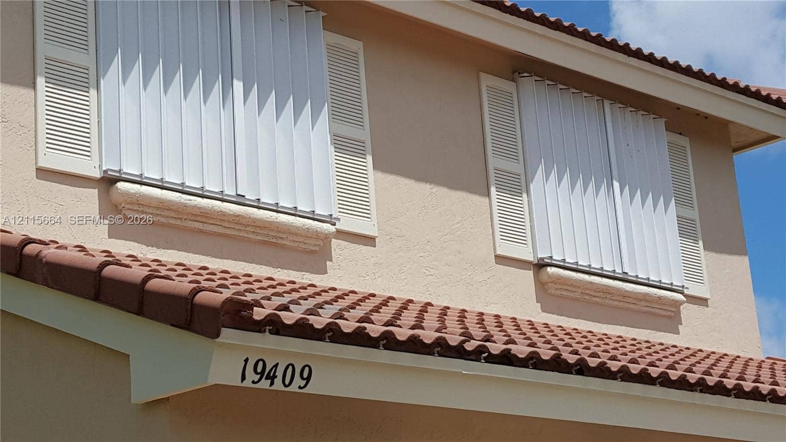 19409 NW 24th Place, Pembroke Pines, FL 33029 Exterior facade featuring a stucco finish, multi-level terra cotta tile roofing, louvered shutters, and metal storm shutters