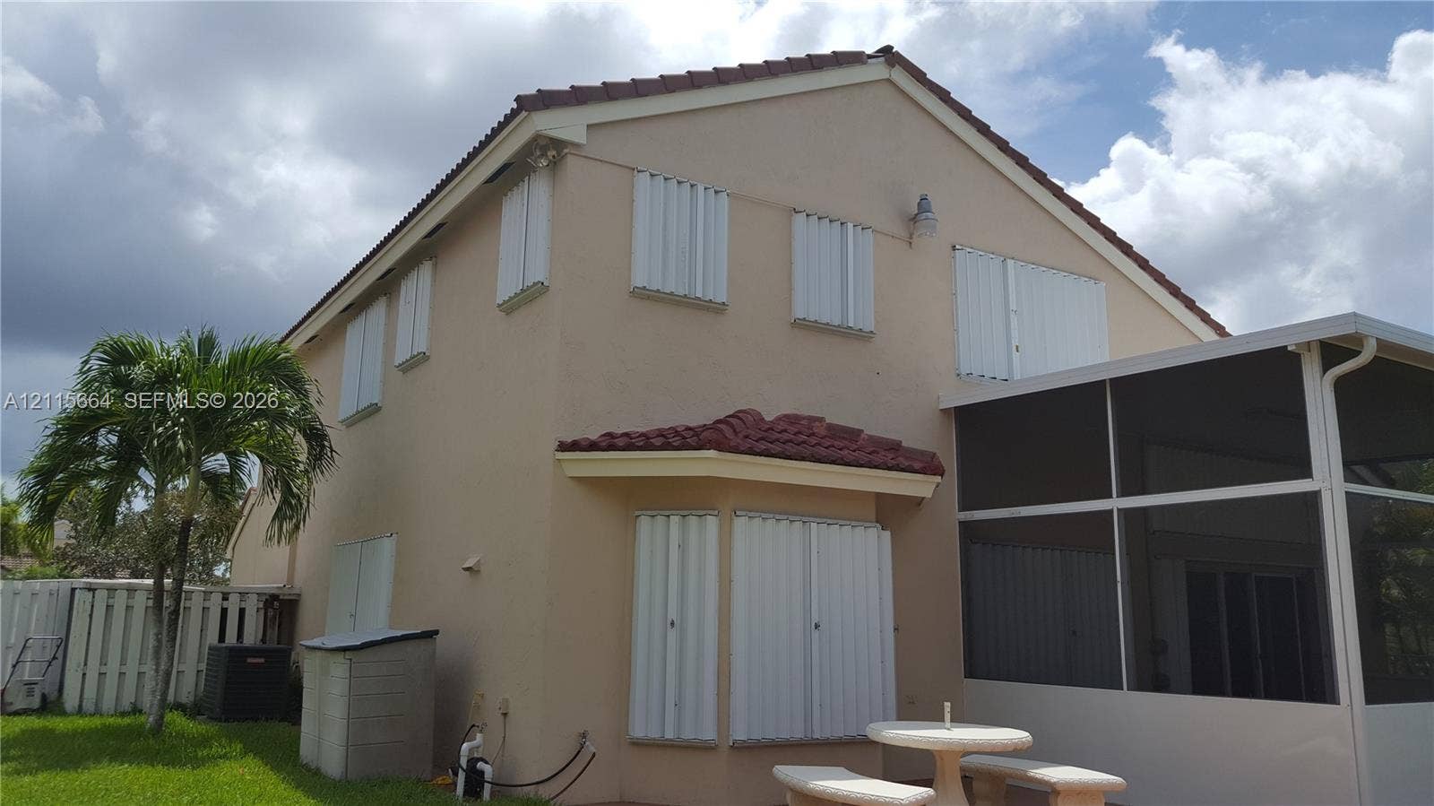 19409 NW 24th Place, Pembroke Pines, FL 33029 Stucco exterior featuring a multi-gable roof line with red tile accents, installed storm shutters, and an enclosed screen lanai