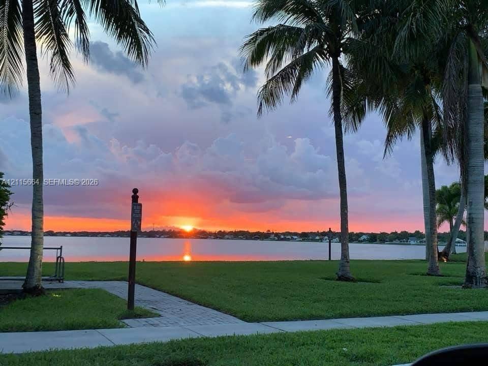 19409 NW 24th Place, Pembroke Pines, FL 33029 Waterfront property featuring manicured lawn, established palm trees, paved walkway, and direct water access