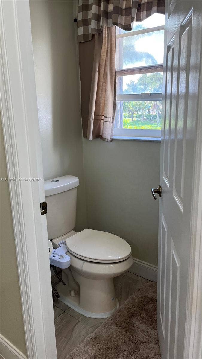 19409 NW 24th Place, Pembroke Pines, FL 33029 Neutral-toned bathroom featuring a two-piece elongated toilet, single-hung window, and tile flooring