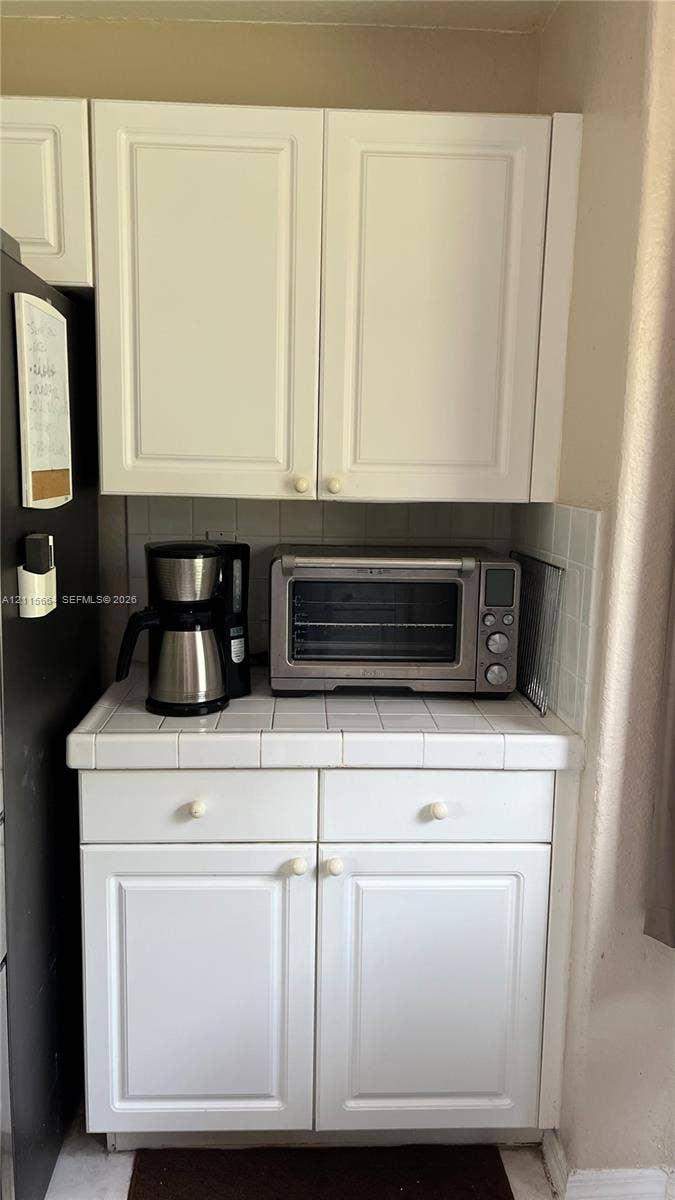 19409 NW 24th Place, Pembroke Pines, FL 33029 White cabinetry with traditional recessed-panel doors, square ceramic tile countertops, and integrated tile backsplash