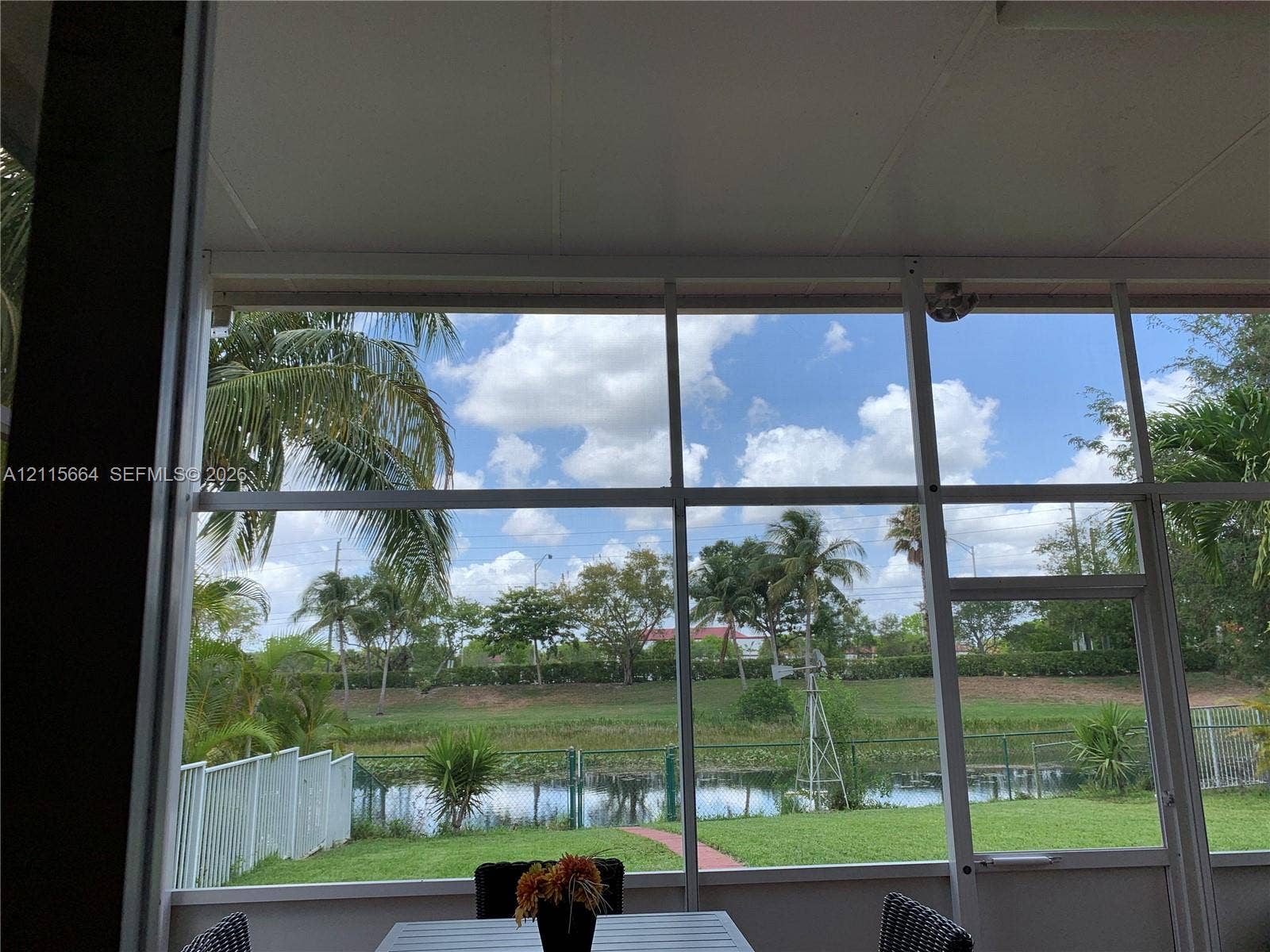 19409 NW 24th Place, Pembroke Pines, FL 33029 Screened-in patio featuring a white frame enclosure, metal ceiling, and a direct line of sight to a pond and manicured lawn