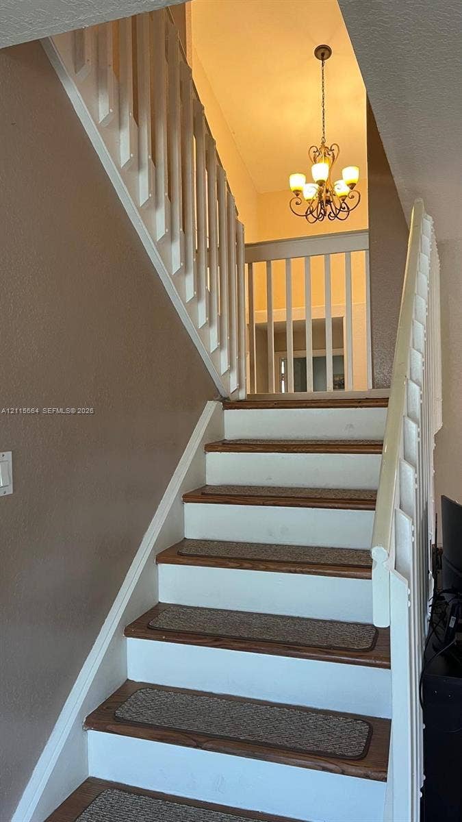 19409 NW 24th Place, Pembroke Pines, FL 33029 Staircase featuring wood-finish treads, white risers, and white vertical balusters with a matching handrail, complemented by a tiered metal chandelier