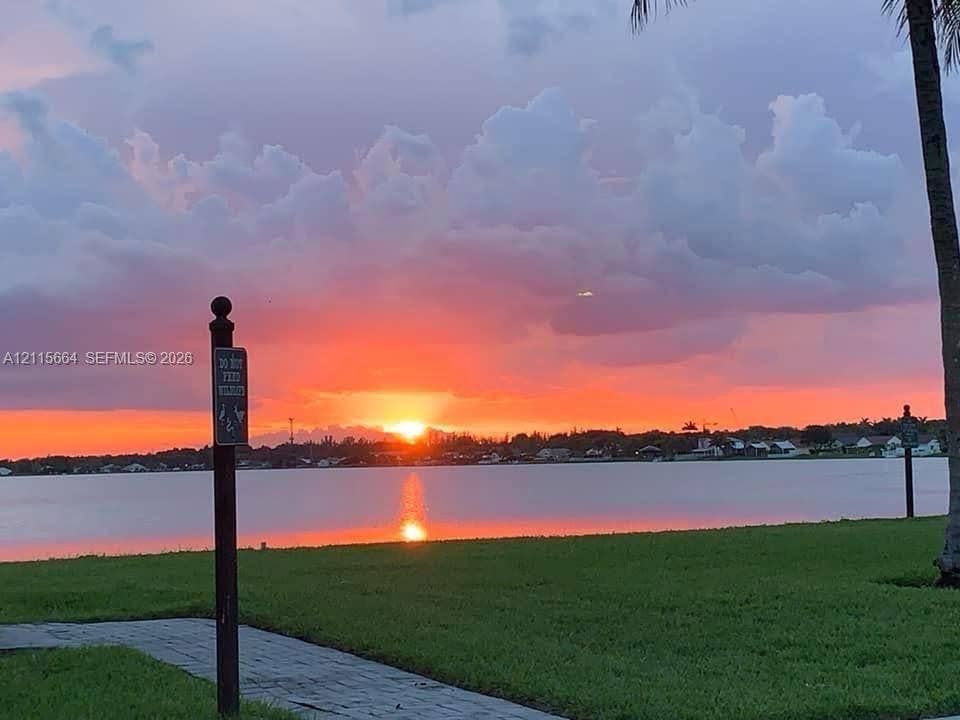 19409 NW 24th Place, Pembroke Pines, FL 33029 Waterfront property featuring a manicured lawn, paved walkway, and natural backdrop