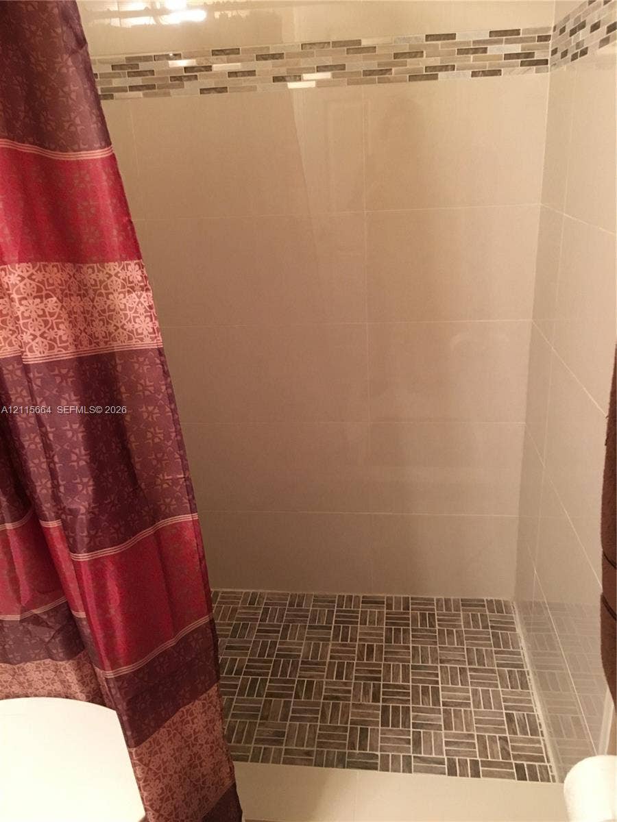 19409 NW 24th Place, Pembroke Pines, FL 33029 Shower stall featuring large-format wall tile, a textured stone-finish floor, and a decorative tile accent border