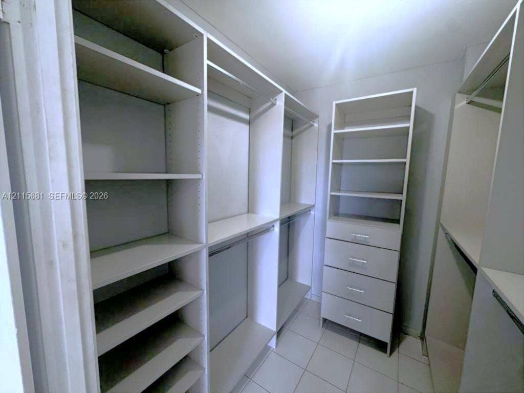 Custom walk-in closet featuring white built-in shelving, integrated hanging rods, and a four-drawer storage unit with tiled flooring