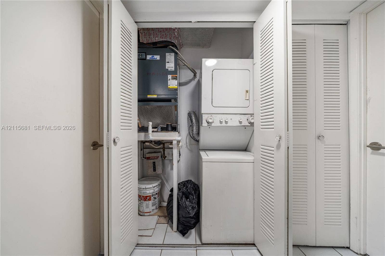 Utility closet featuring louvered bi-fold doors, stacked laundry appliance, and an integrated heating system