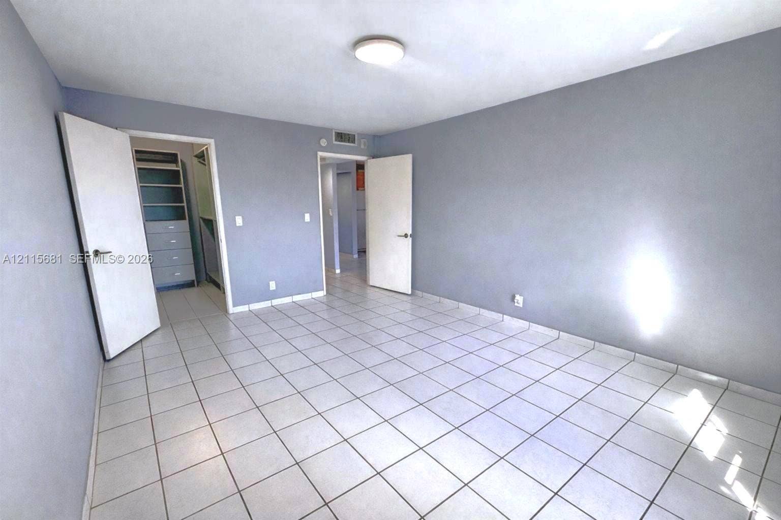 Room featuring light-toned tile flooring, neutral wall paint, and a built-in closet with integrated shelving and drawer storage