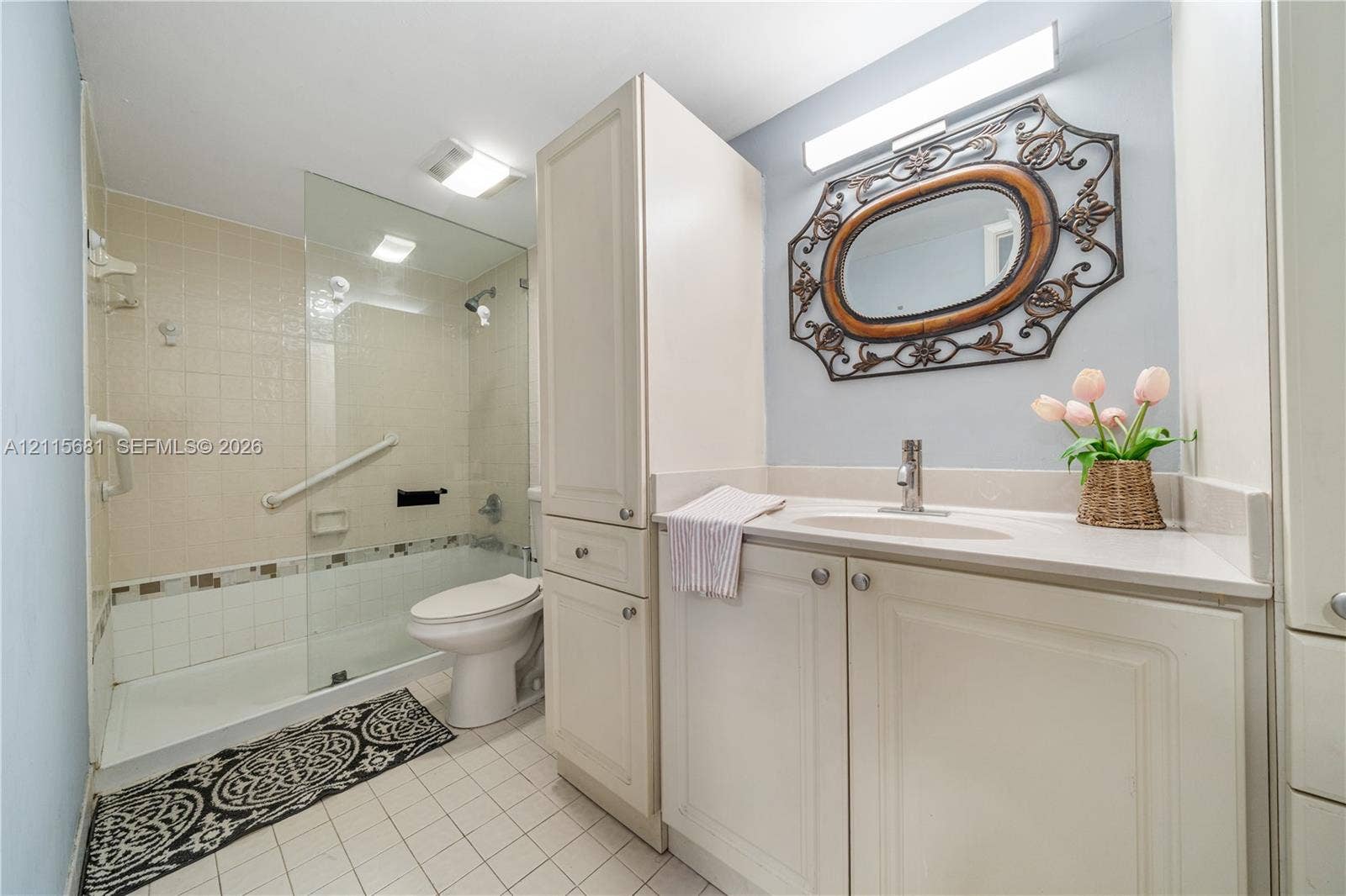 Bathroom featuring a built-in white vanity with integrated cabinetry, a glass-enclosed shower, wall-mounted hardware, and tile flooring